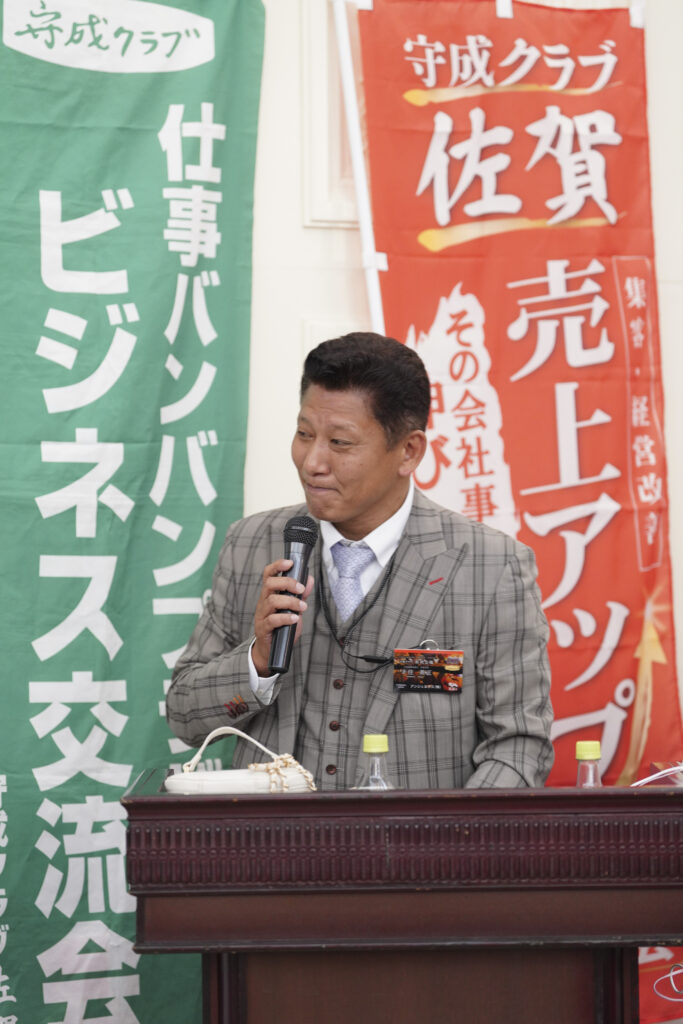 守成クラブ佐賀の旗の前で挨拶する登壇者